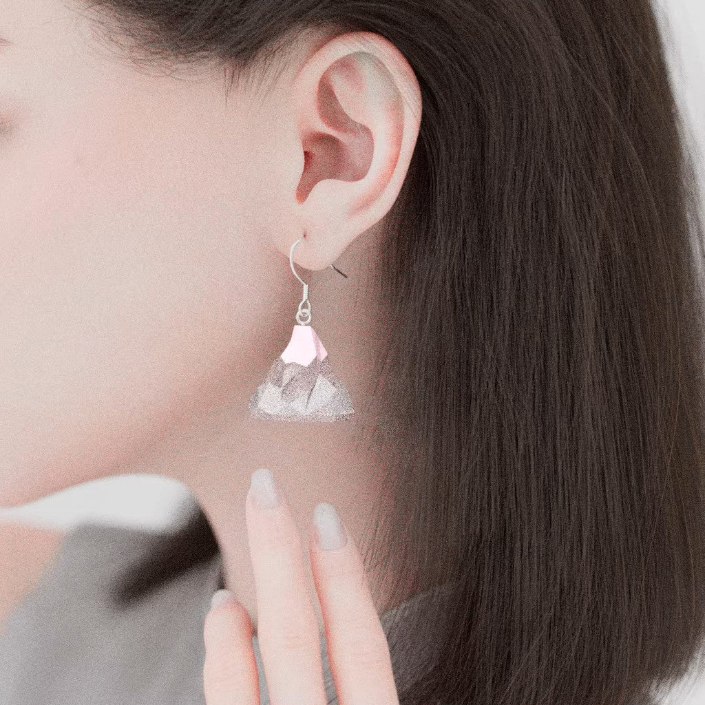 Mismatched Arctic Drift earrings featuring a geometric penguin standing on a floating iceberg and a separate faceted iceberg charm, worn on silver hooks.