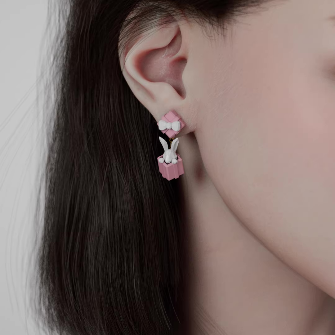 Pastel pink gift box earrings with a white bow and a small bunny figure popping out, cute handmade acrylic jewelry shown from multiple angles
